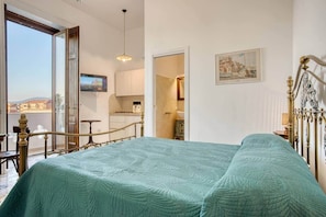 Una camera da letto con un letto, una TV, un balcone e un angolo cottura.