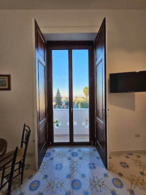 Una porta aperta che dà su un balcone con vista sulla città, una sedia e un tavolo.