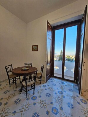 Un espace repas avec une table ronde et des chaises, une porte donnant sur l’extérieur et un sol à motifs.