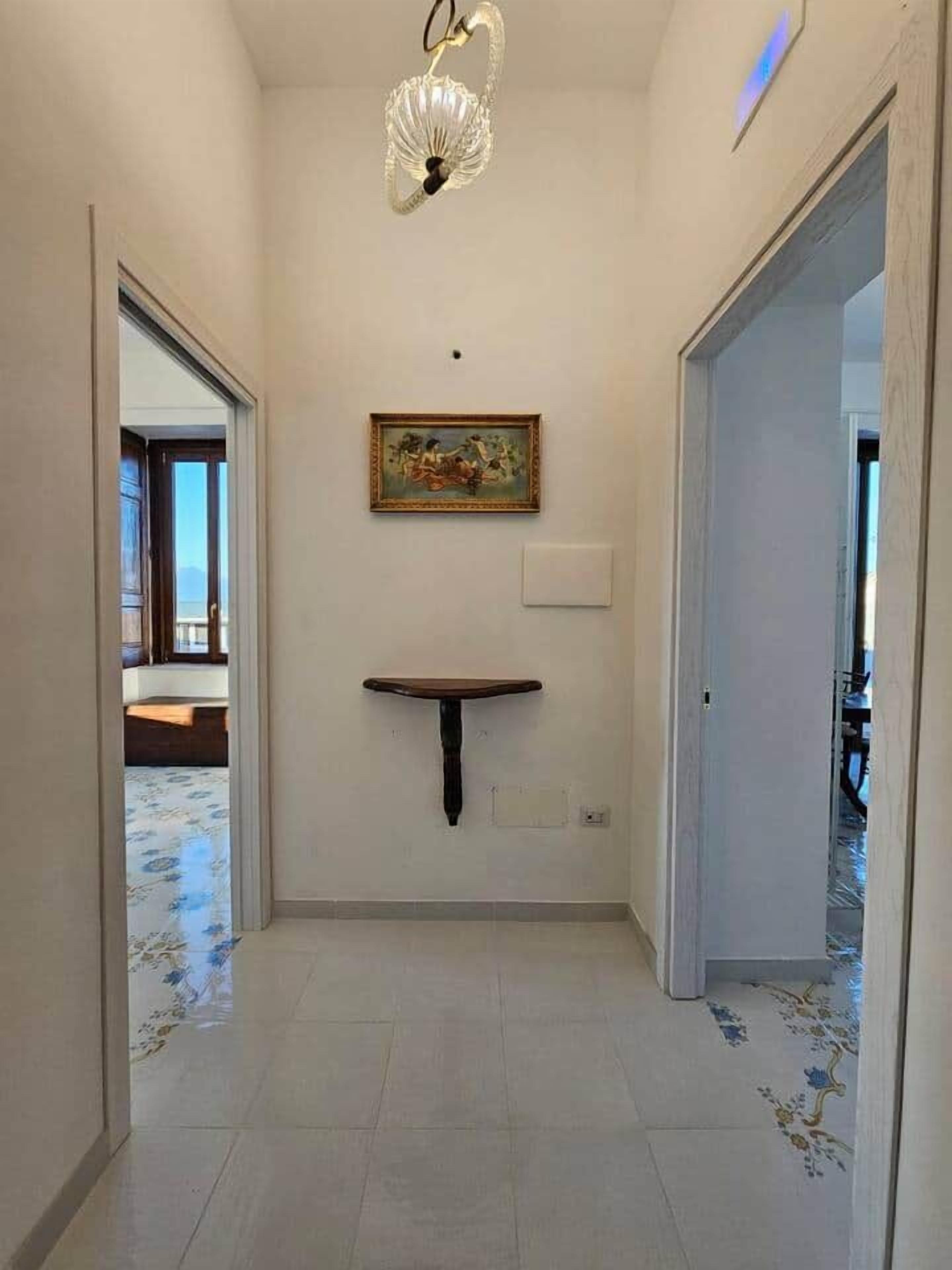 Um corredor com prateleira na parede, um quadro e luminária no teto.