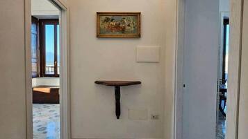 Um corredor com prateleira na parede, um quadro e luminária no teto.