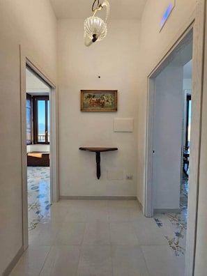 Un couloir avec une étagère fixée au mur, un tableau et un luminaire au plafond.