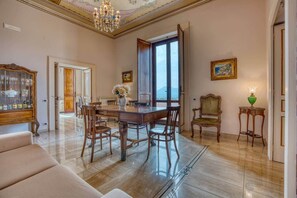 Ein geräumiges Zimmer mit einem Holzespeisesaal, Stühlen, einer Couch, einem Kronleuchter und Blick durch ein großes Fenster.