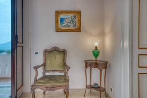 Ein Zimmer mit einem Holzsessel, einem Tisch mit einer grünen Lampe und einem gerahmten Gemälde an der Wand.