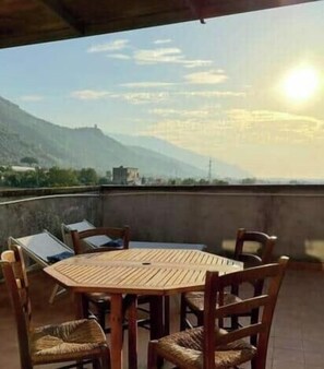 Ein runder Holztisch mit Stühlen auf einer Terrasse mit Blick auf die Berge.