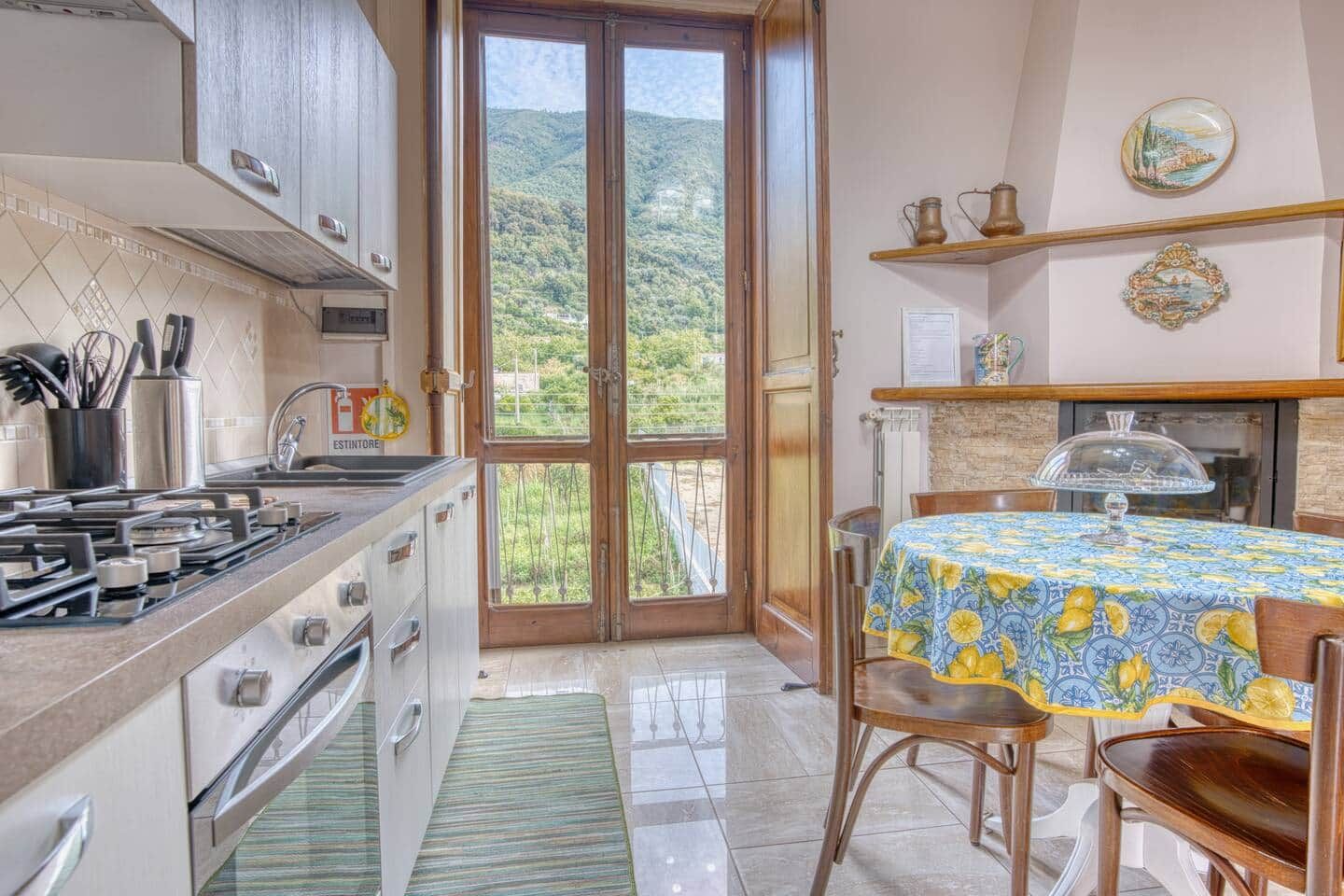 Una cocina con estufa a gas, un lavamanos y vista a un paisaje montañoso a través de un ventanal.