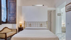 A bedroom with a bed, a nightstand, a lamp, a chair, and a window with curtains. - Il Mosaico Family Home near Pompeii (Angri)