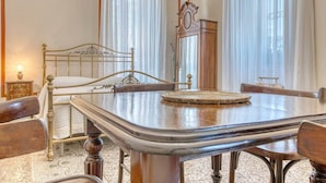 A room with a bed, a wooden table, chairs, a clock, and a window with curtains. - Il Mosaico Family Home near Pompeii (Angri)