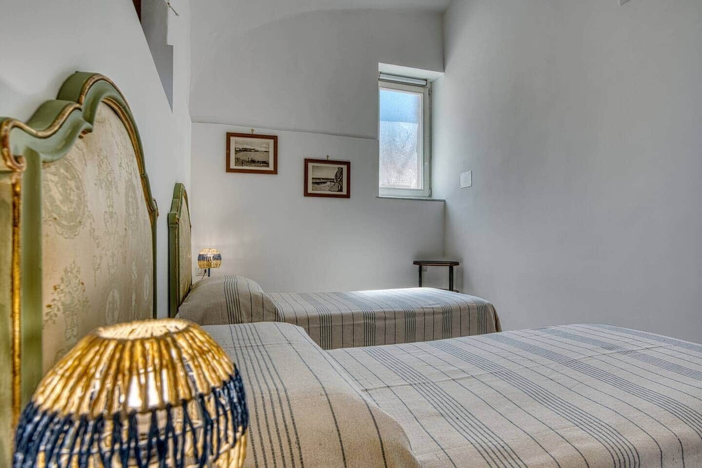 A room with two beds, a lamp, a small table, and two framed pictures on the wall.