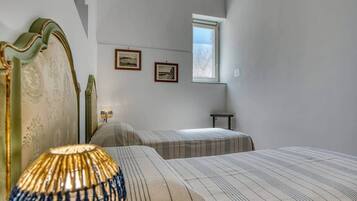A room with two beds, a lamp, a small table, and two framed pictures on the wall.