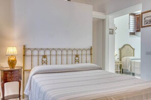 Una camera da letto con un letto, un comodino con una lampada, una sedia e una porta che dà su un'altra stanza.