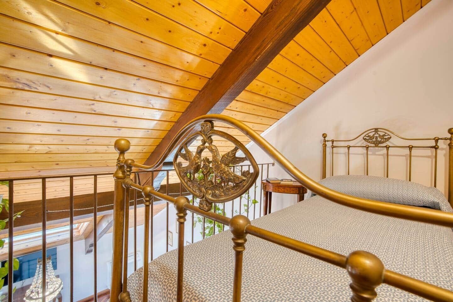 A bedroom with a wooden ceiling, a bed with a metal headboard, and a balcony with a railing.