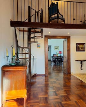 Una scala in legno conduce a una zona mansardata con una sedia, un tavolo da pranzo e sedie sullo sfondo.