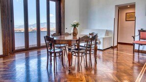 A dining area with a wooden table and chairs, a vase with flowers, and a view through large windows. - Historic Villa Apartment with Panoramic Views of Mount Vesuvius (Angri)
