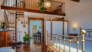 A bedroom with a four-poster bed, a wooden staircase, and a dining area in the background. - Historic Villa Apartment with Panoramic Views of Mount Vesuvius (Angri)