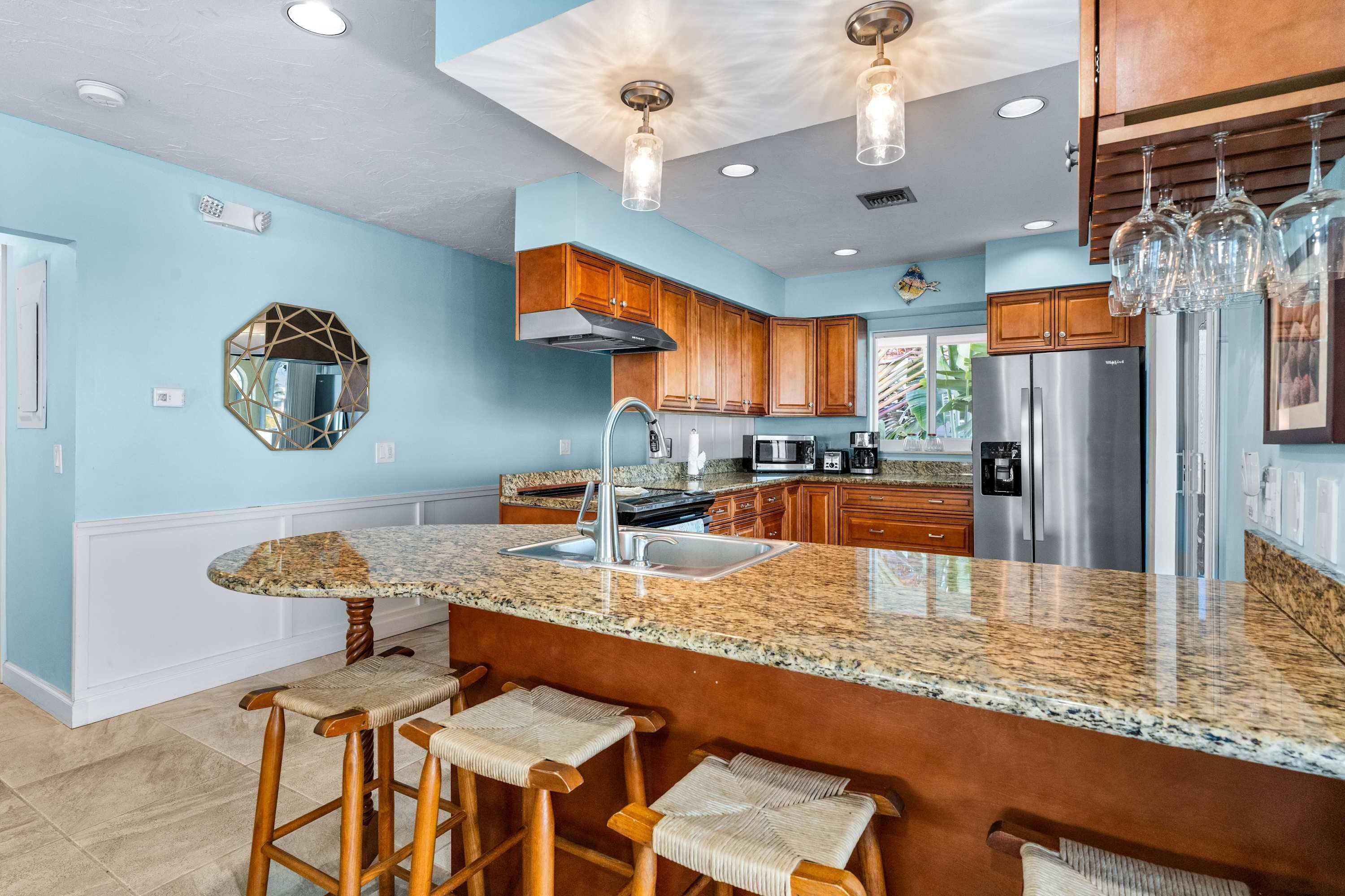 A modern kitchen with granite countertops, wooden bar stools, stainless steel appliances, and a large island.
