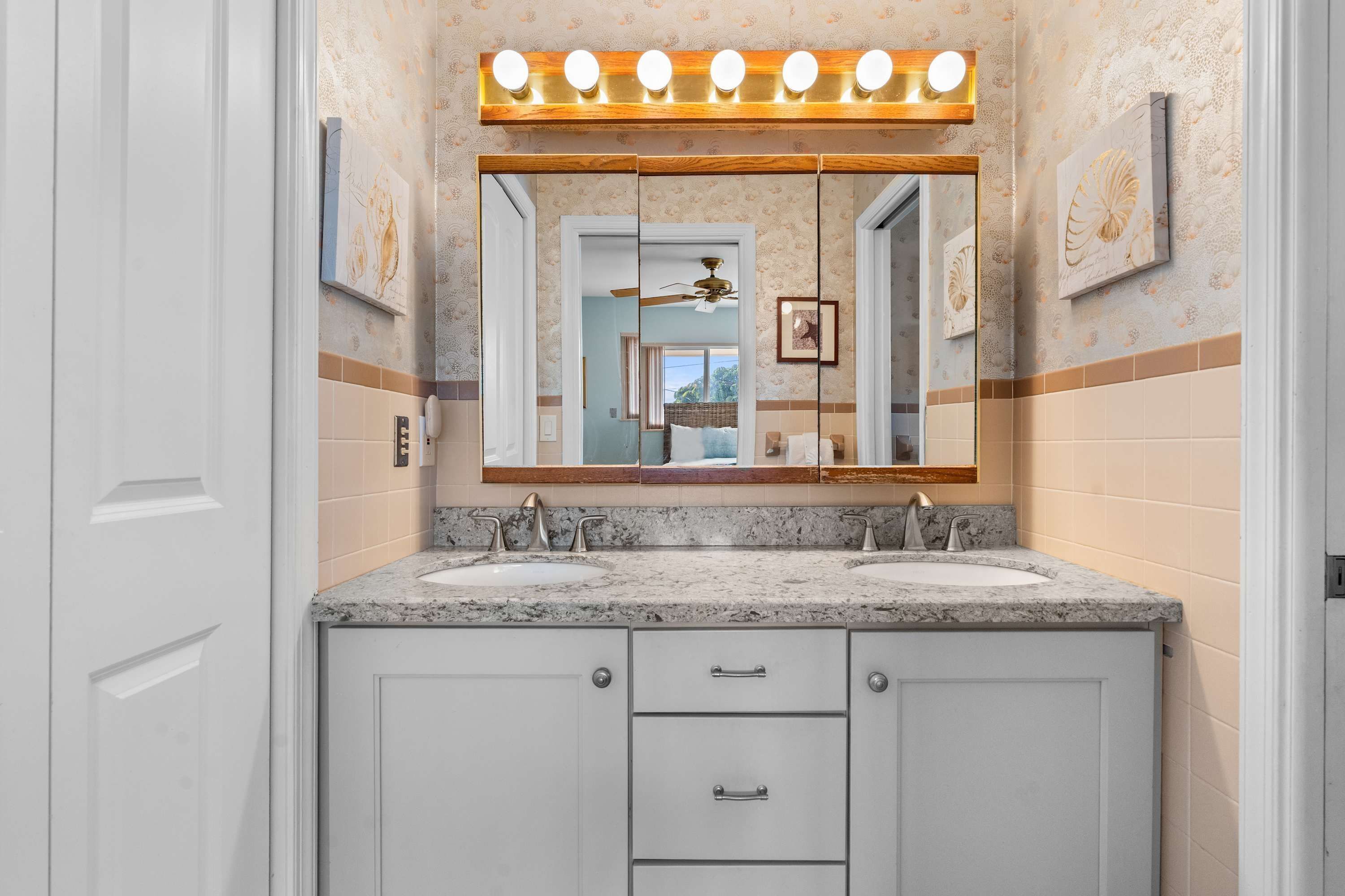 Une salle de bain avec un meuble-lavabo, deux éviers, un miroir avec éclairage intégré et un ventilateur de plafond.