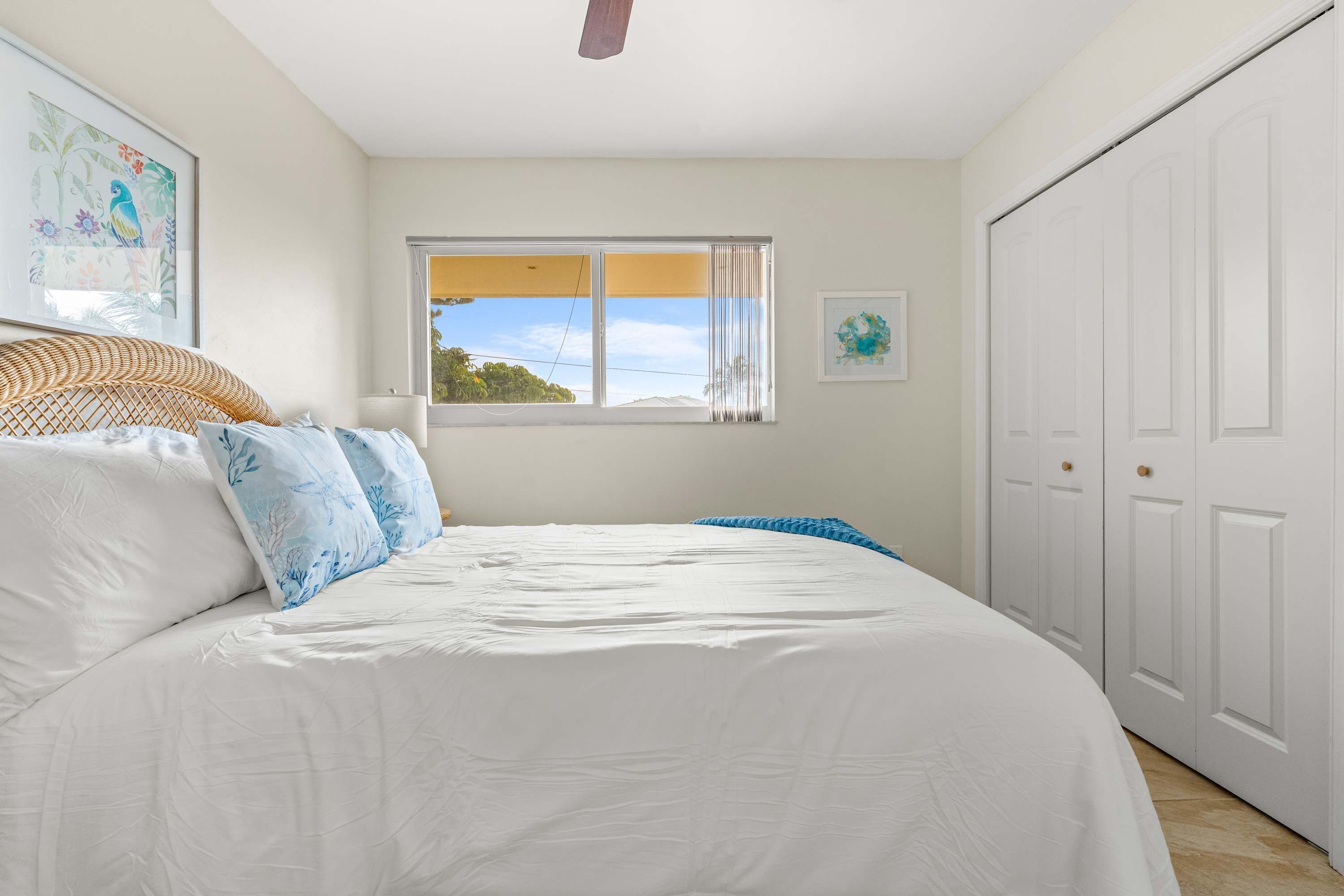 Une chambre à coucher avec un grand lit, une fenêtre avec des rideaux, une armoire blanche et un ventilateur de plafond.