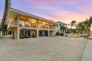 A two-story building with a covered patio area, multiple seating arrangements, and a staircase leading to an upper level. - Sunset Harbor Waterfront Villa With Dock Cabana Club (Key Colony Beach)