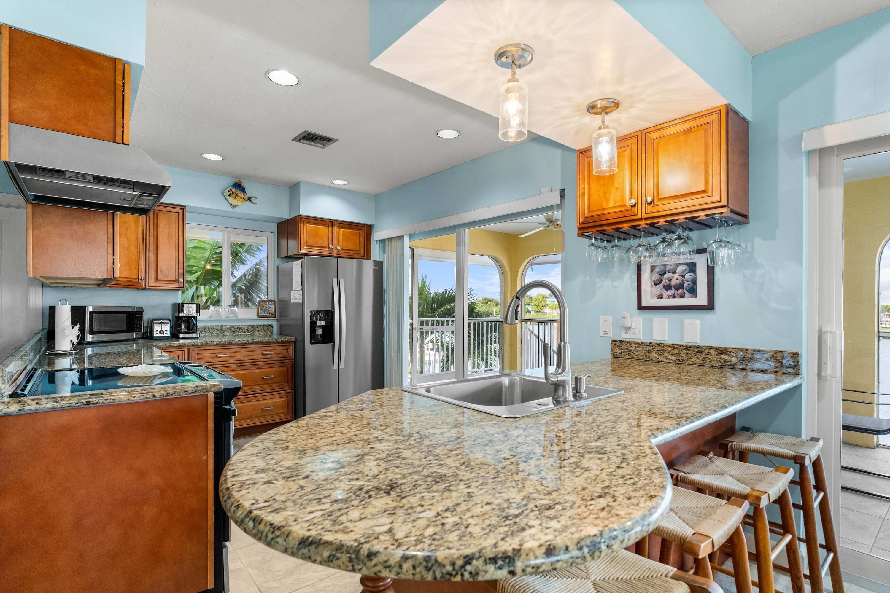 A kitchen with granite countertops, wooden cabinets, stainless steel appliances, and a bar area with stools.