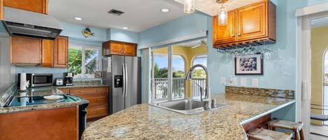 A kitchen with granite countertops, wooden cabinets, stainless steel appliances, and a bar area with stools.
