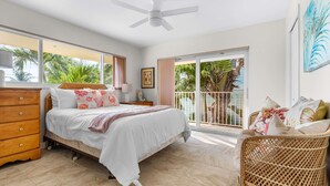 Un dormitorio con cama, cómoda, mesita de noche y un balcón con vista a palmeras.