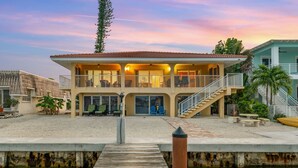 Una propiedad frente al agua, con un muelle de madera que conduce a una casa con varios balcones y un patio cubierto.
