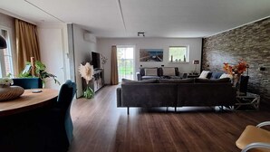 Un salon moderne avec un canapé gris foncé, un plancher en bois, un coin repas comprenant une table et des chaises, et un mur en pierre.