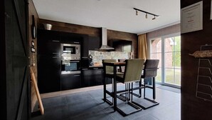 Une cuisine moderne avec des meubles de couleur sombre, un four encastré et un coin repas comprenant deux chaises et une table.