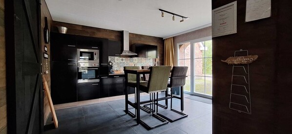 A modern kitchen with dark cabinetry, a built-in oven, and a dining area with two chairs and a table.