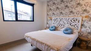 A bedroom with a bed, a window, a patterned wallpaper, and a nightstand with a lamp. - First A - La Torre de Suances (Suances)