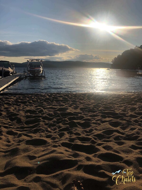 Una playa con barcos amarrados, una orilla arenosa y una puesta de sol al fondo.