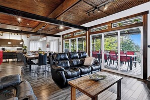 A spacious living area with a leather sofa, dining table, and a view through large glass doors to an outdoor patio.