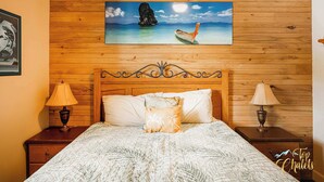 A bedroom with a wooden headboard, a bed with a patterned bedspread, two nightstands with lamps, and a painting of a tropical scene above the bed. - LAKE Simon, SPA, private BEACH, 4 bedroom, 2 private office, 10 beds, 16 people. (Lac-Simon)