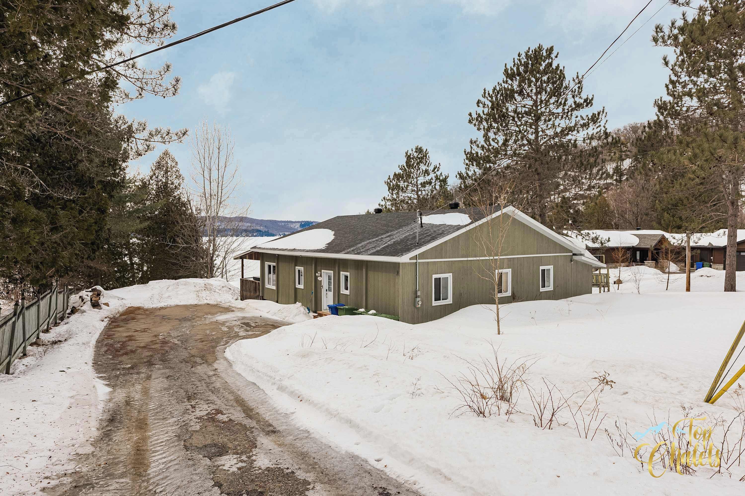 Une maison de plain-pied avec un toit en pente, entourée d’un paysage enneigé et d’arbres.