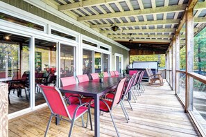 A covered outdoor dining area with a long table and red chairs, surrounded by glass doors and windows.