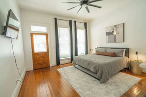 Een slaapkamer met een bed, een plafondventilator, een deur en een raam met gordijnen.
