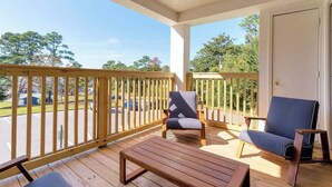 A wooden deck with two chairs and a table, overlooking a parking lot and trees. - Fly Creek Collection - Bluff View (Fairhope)