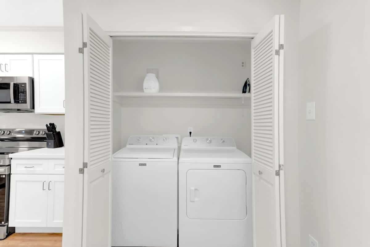 Un cuarto de lavandería con dos lavadoras y secadoras de carga frontal blancas, un microondas y un armario blanco.