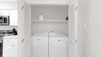 Un cuarto de lavandería con dos lavadoras y secadoras de carga frontal blancas, un microondas y un armario blanco.