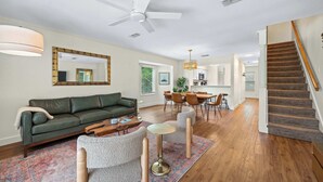 A living room with a green sofa, a coffee table, a round table, and a staircase. - Fly Creek Collection - Bluff View (Fairhope)