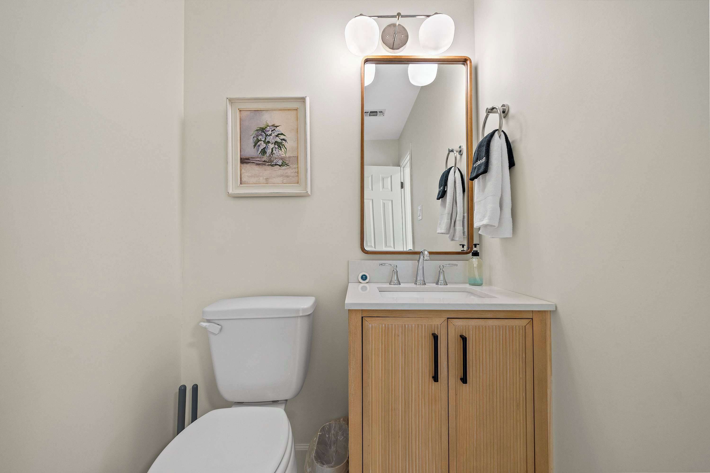 Ein Badezimmer mit Toilette, einem Waschbecken mit Spiegel darüber und einem gerahmten Bild an der Wand.