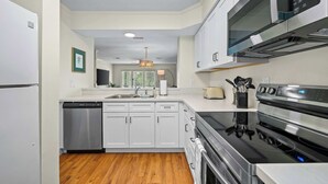 A modern kitchen with stainless steel appliances, white cabinetry, and a wooden floor. - Fly Creek Collection - Bluff View (Fairhope)