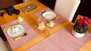Een keurig gedekte tafel met een camera, laptop, borden, bestek en een kleine plant.