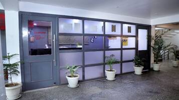 Entrada de hotel com porta cinzenta, várias janelas e plantas em vasos.