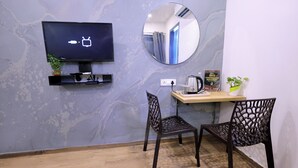 Huoneessa on seinälle asennettu televisio, pyöreä peili, kaksi tuolia, pieni pöytä, jossa on kahvinkeitin, ja huonekasvi.