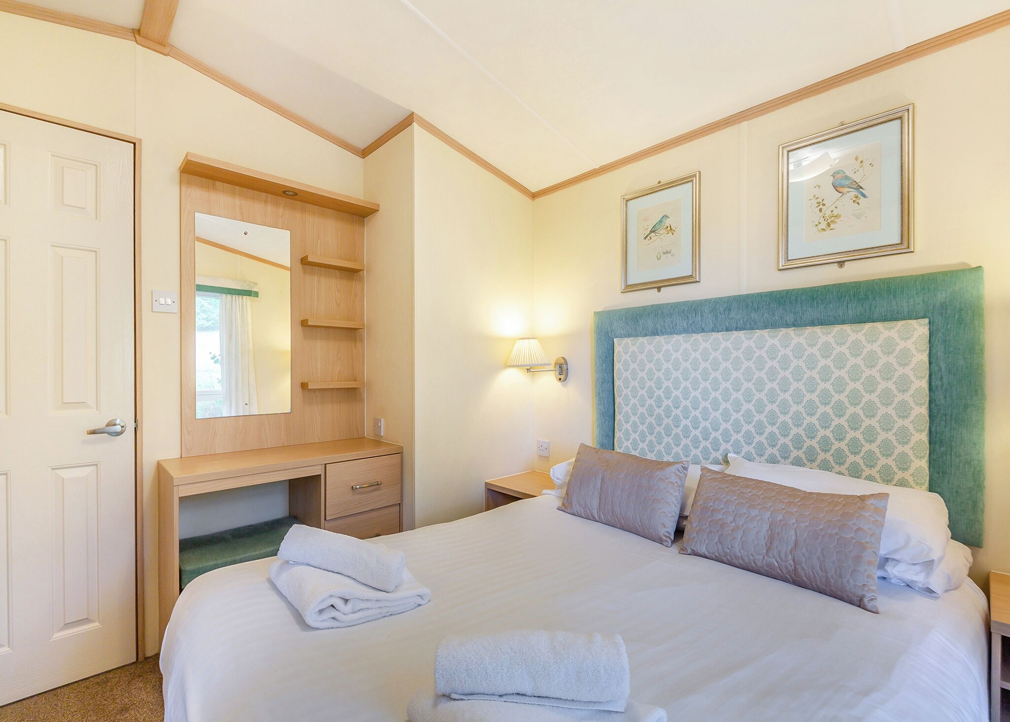 A hotel room with a bed, a desk, a mirror, and two framed pictures on the wall.