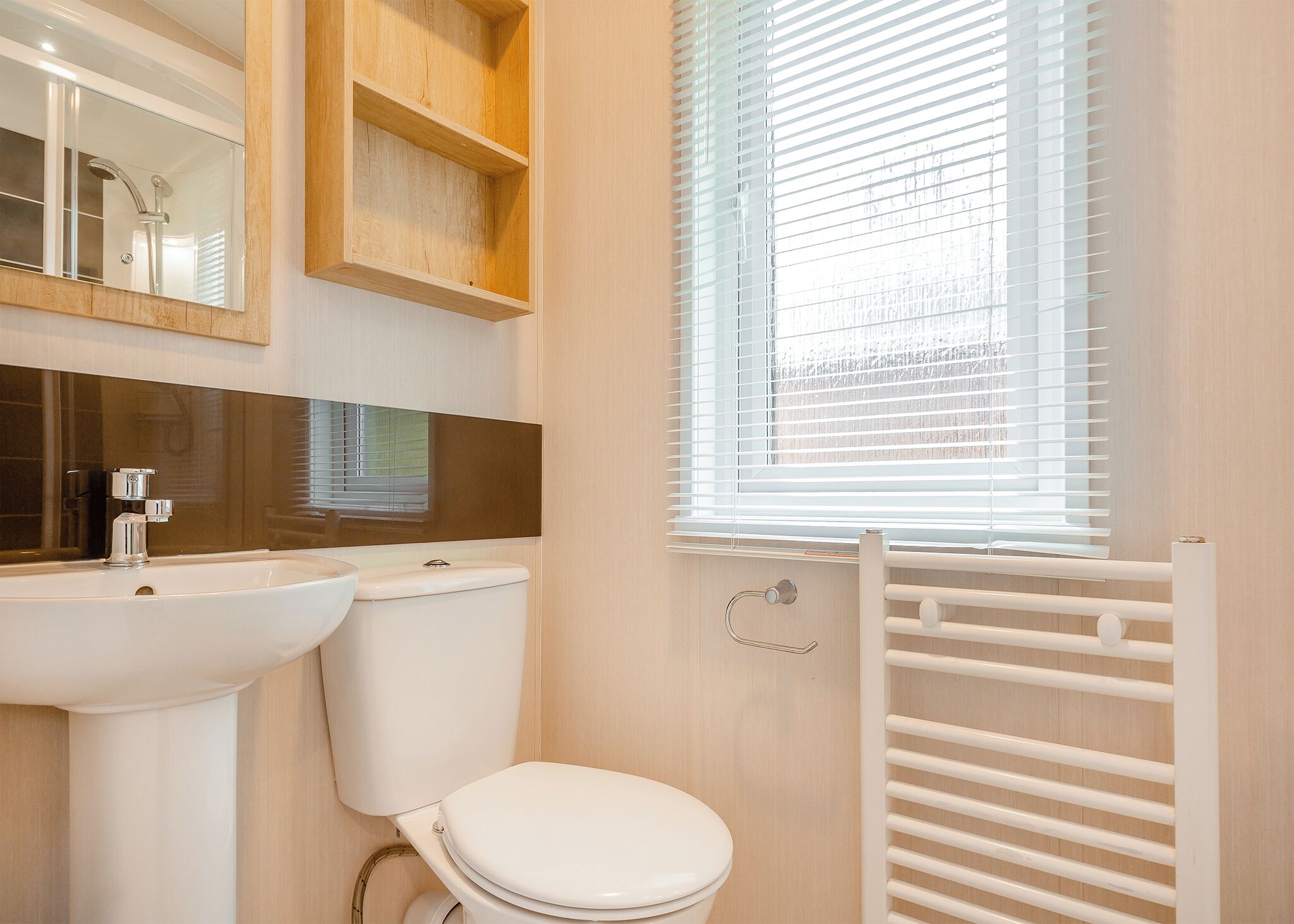 Een badkamer met een wastafel, toilet, spiegel en raam met zonwering.