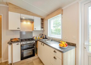 A compact kitchen with a gas stove, oven, and a window with blinds. - Foxglove 4 Platinum (Pet) (Bala,)