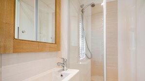 Een badkamer met een wit wastafel, een spiegel en een douche met een glazen deur.